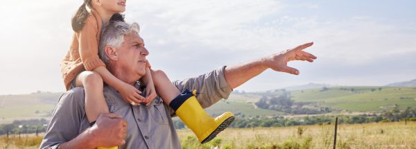 Older man with a child wearing yellow boots on his shoulders, looking out to the horizon