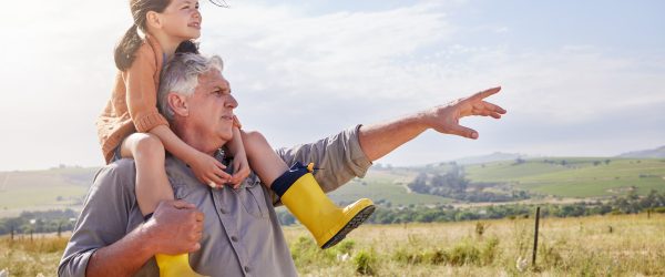 Older man with a child wearing yellow boots on his shoulders, looking out to the horizon